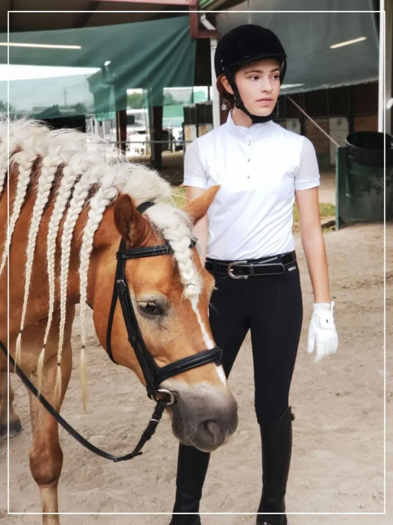 A woman in white shirt and black pants standing next to a horse.