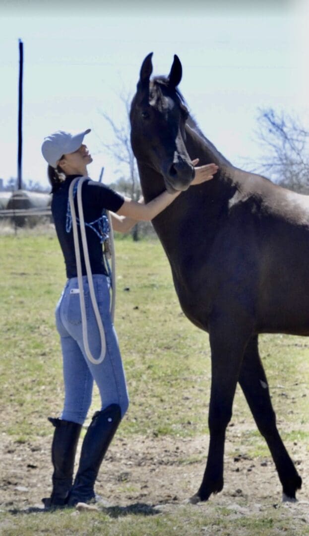 A woman standing next to a horse in the grass.