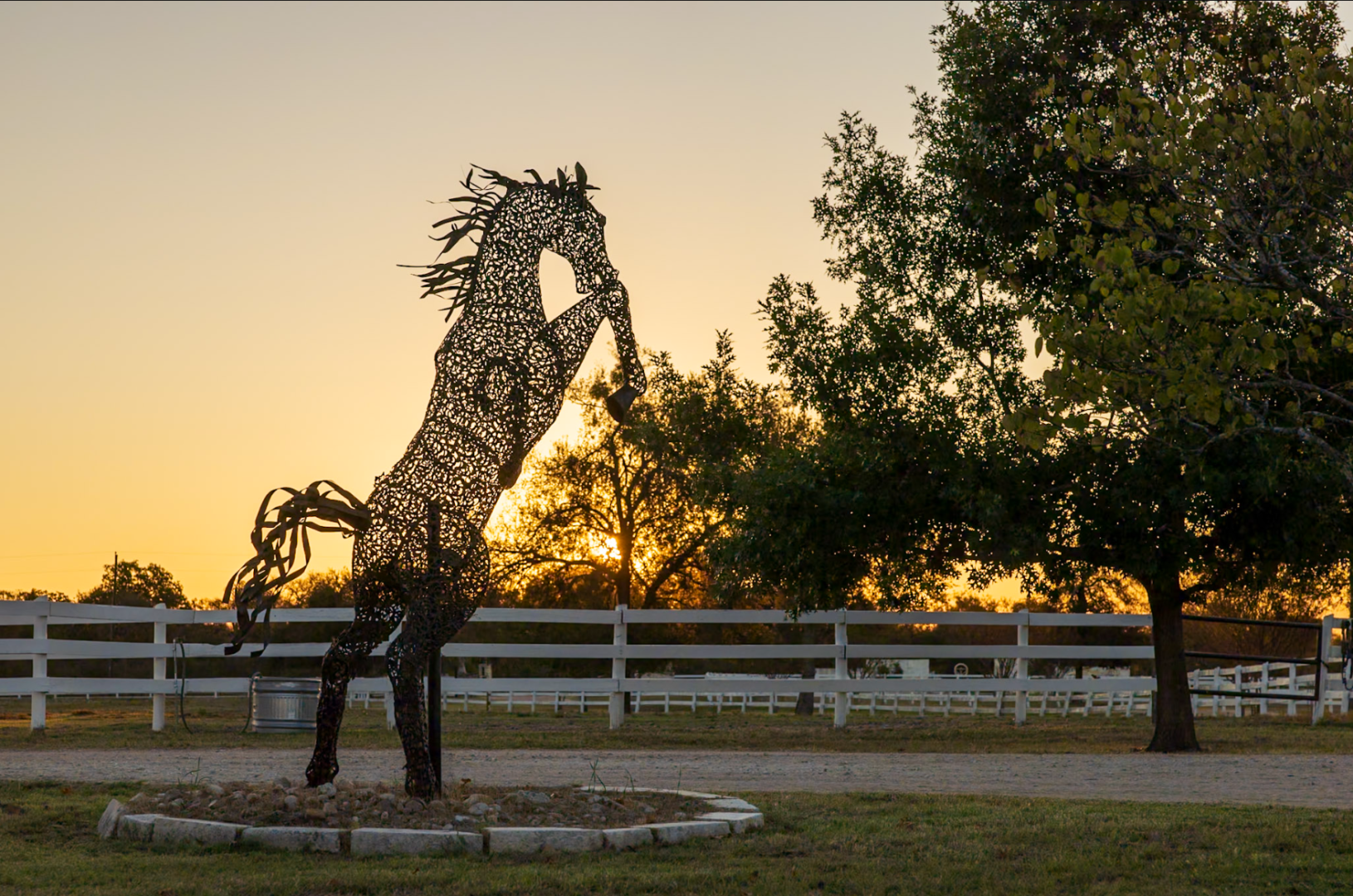 A horse statue in front of a fence and trees.