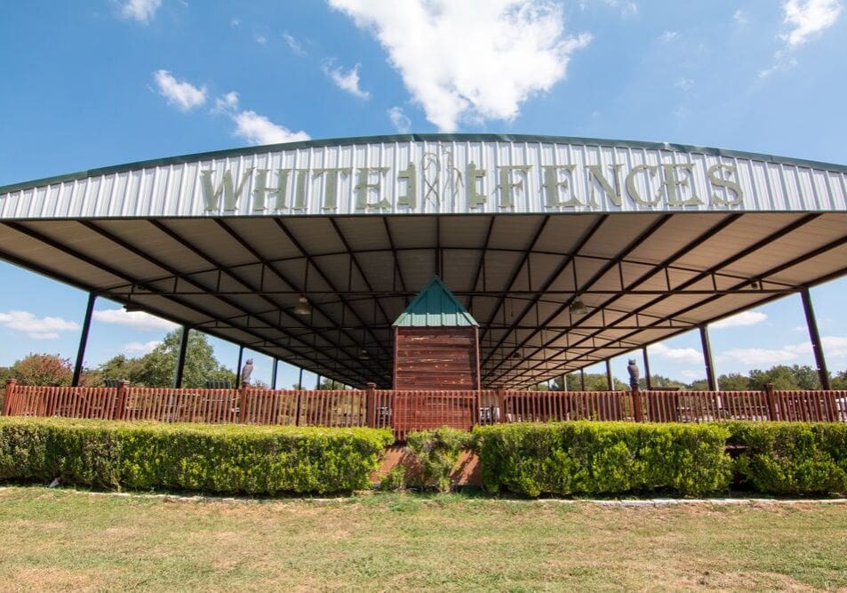 A large building with a fence and bushes around it.